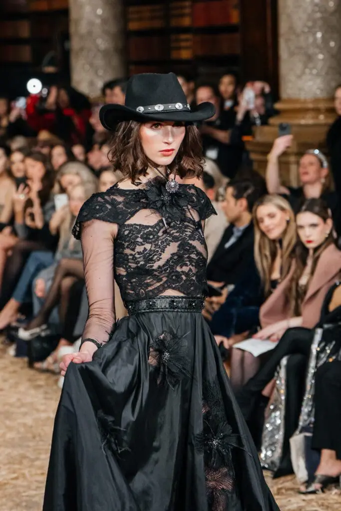 Model in black lace top and full skirt with cowboy hat on a hay-strewn runway