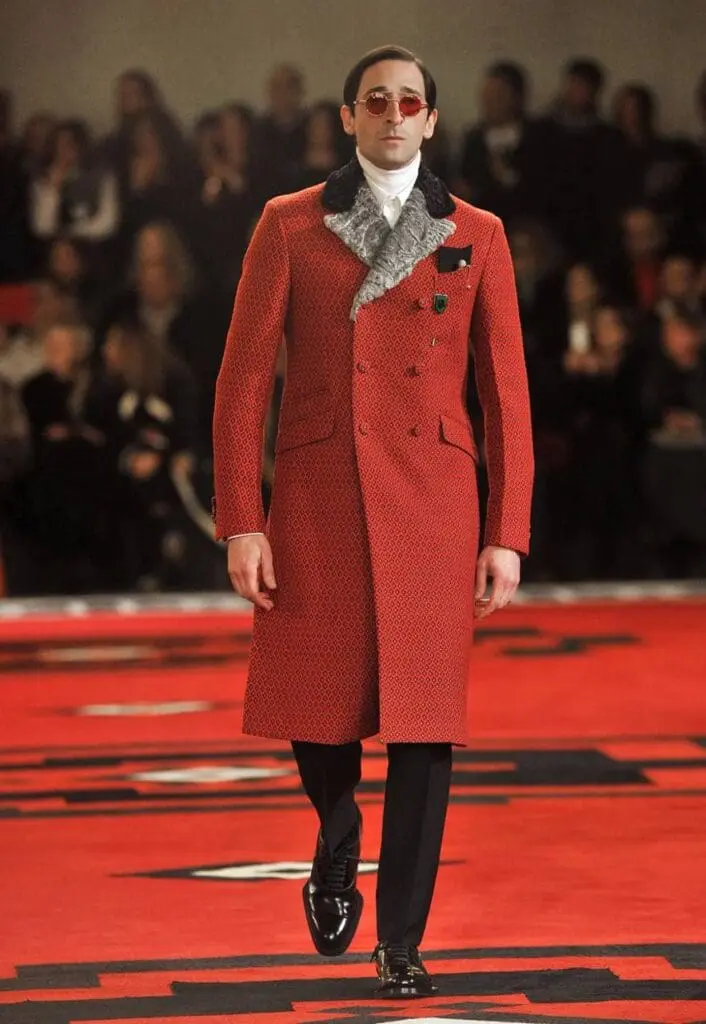 Adrien Brody wearing a red double-breasted coat with fur collar by Prada
