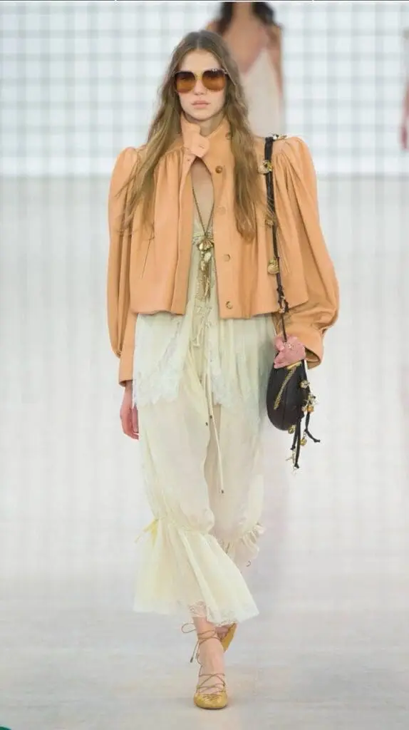 Model in apricot puff-sleeve jacket and flowing ivory skirt