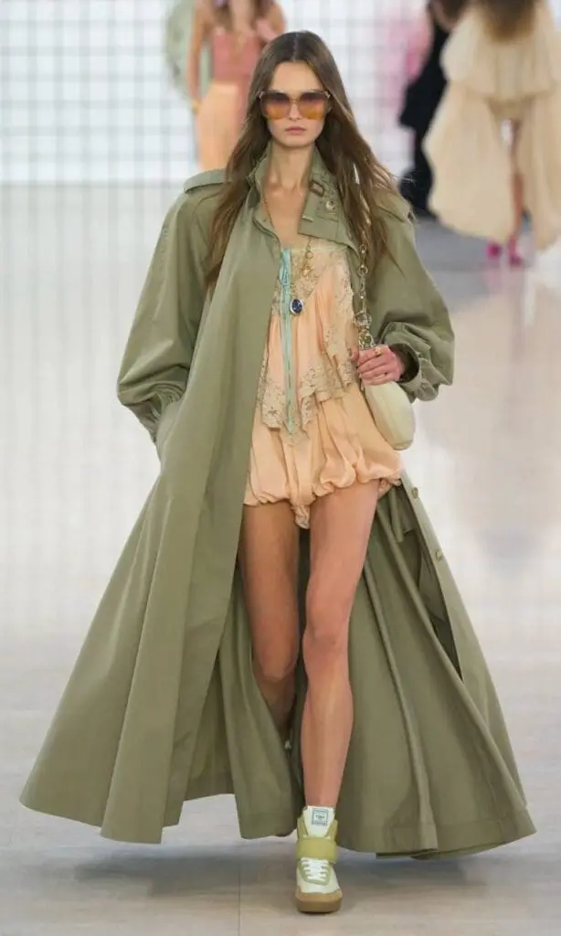 Model wearing peach romper with flowy olive trench and sneakers