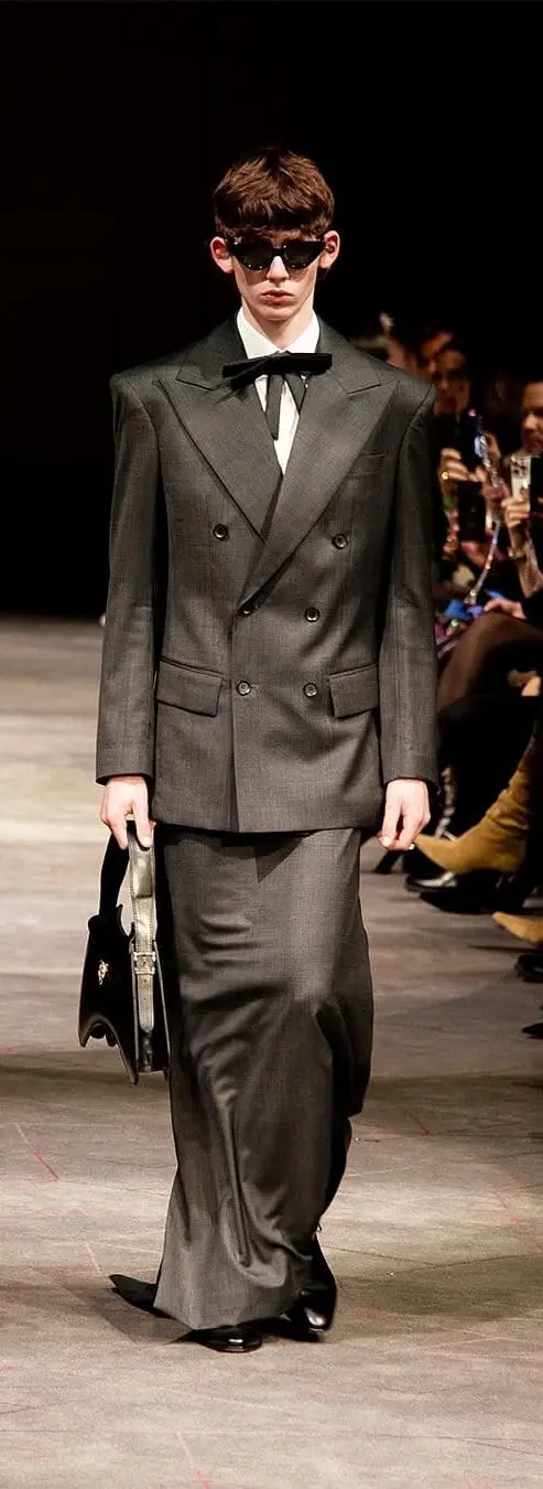 Model in grey double-breasted suit with elongated skirt-trousers walking forward