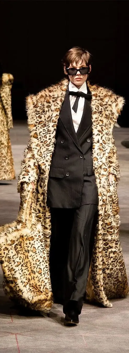 Model in classic tuxedo layered under a full-length leopard print coat, mid-stride on runway