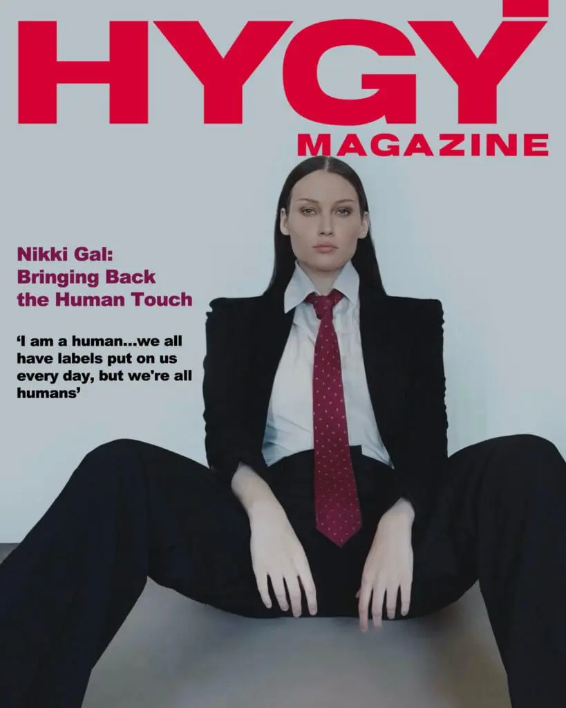 Nikki Gal on the cover of HYGY Magazine wearing a black suit and red tie, challenging fashion norms with her quote about human identity.