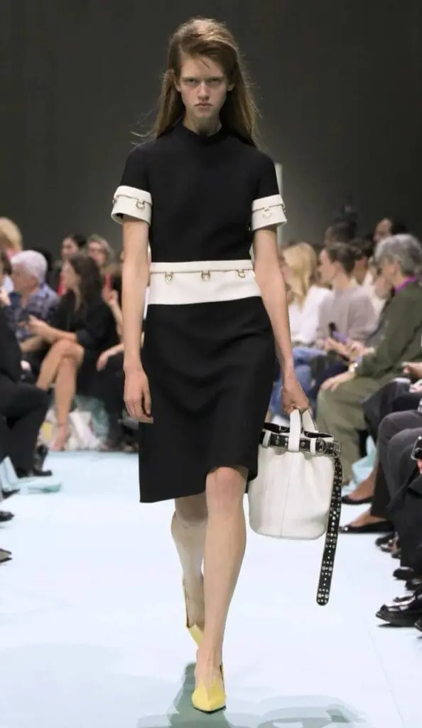 Model in fitted black dress with white belt and structured handbag by Prada