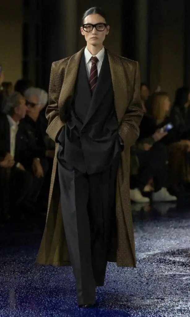 Model in oversized brown coat, black suit, and striped tie from Saint Laurent 2025