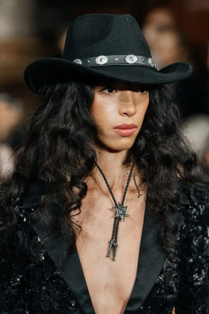 Model in black cowboy hat with bolo tie on runway