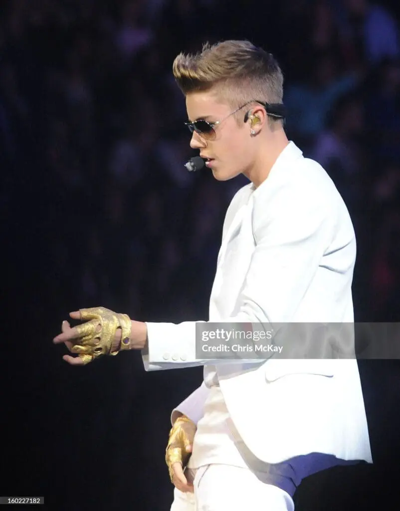 Justin Bieber wearing white suit and gold gloves mid-performance during 2013 concert