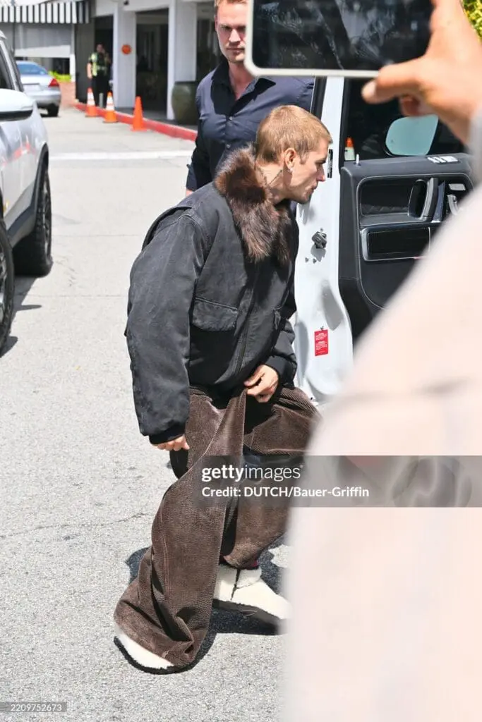 Justin Bieber in wide corduroys and black jacket with fur collar stepping out of a vehicle