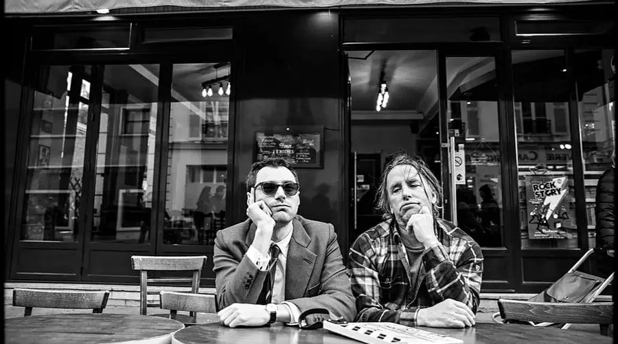Black-and-white photo of Linklater and Guillaume Marbeck seated in front of a cafe