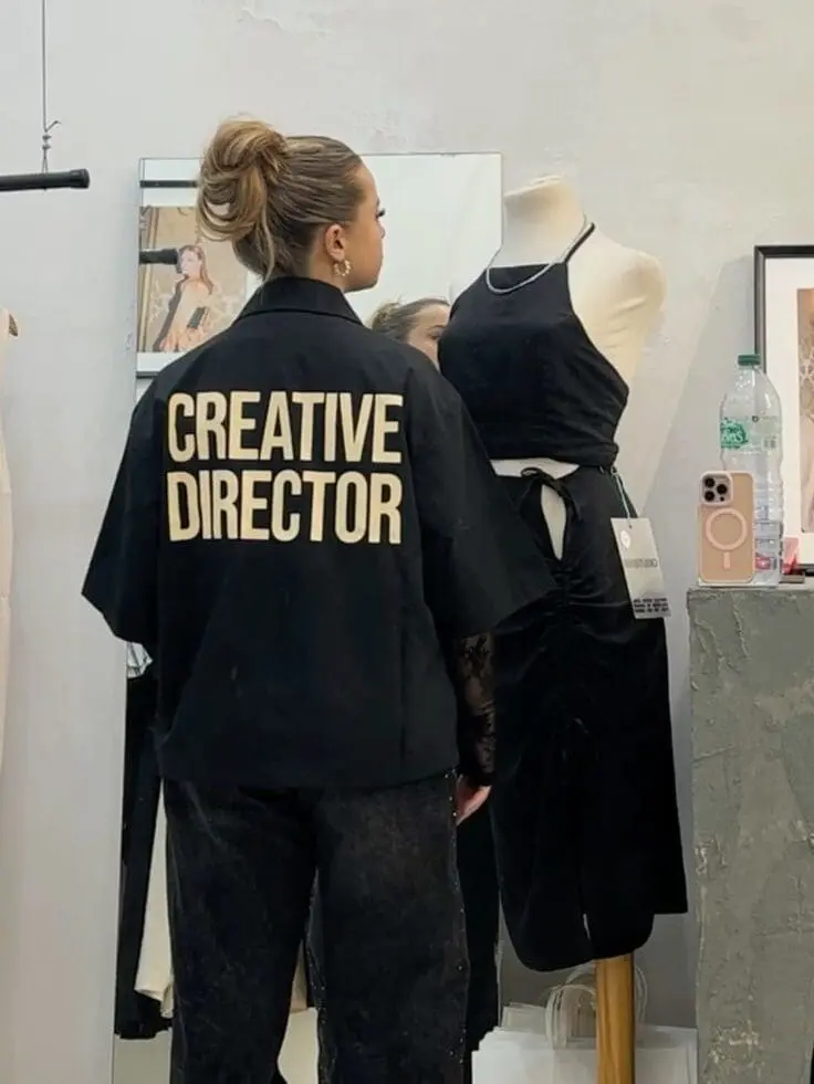Woman in “Creative Director” shirt looking at black dress on mannequin