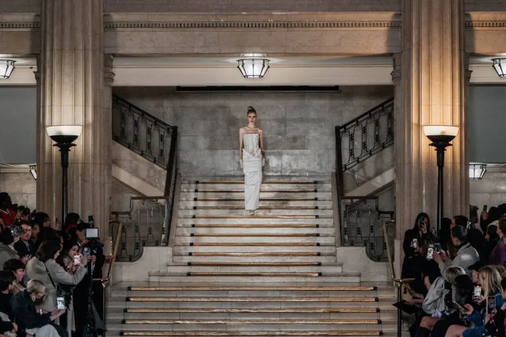 Model in strapless white gown descending grand staircase runway