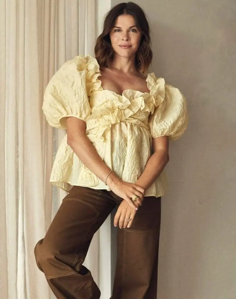 Emily Weiss in a cream ruffled top and brown pants