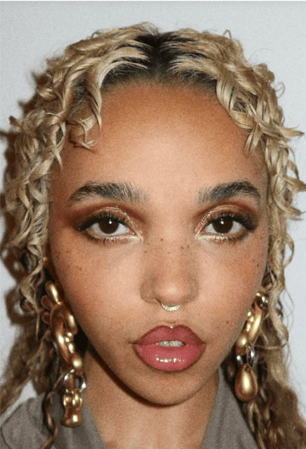 FKA Twigs with shimmery bronze eye makeup, natural freckles, and glossy lips