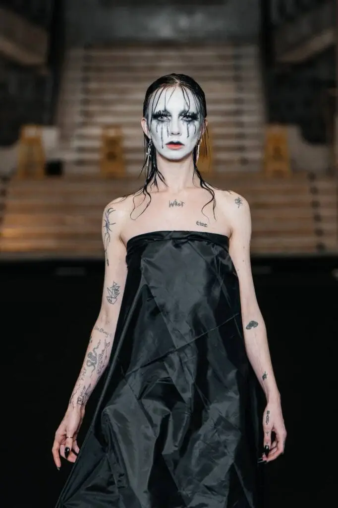 Model with dramatic black-and-white makeup in black draped dress