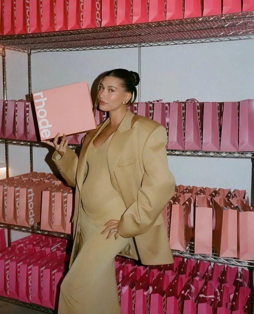Hailey Bieber posing with a pink Rhode box in storage room