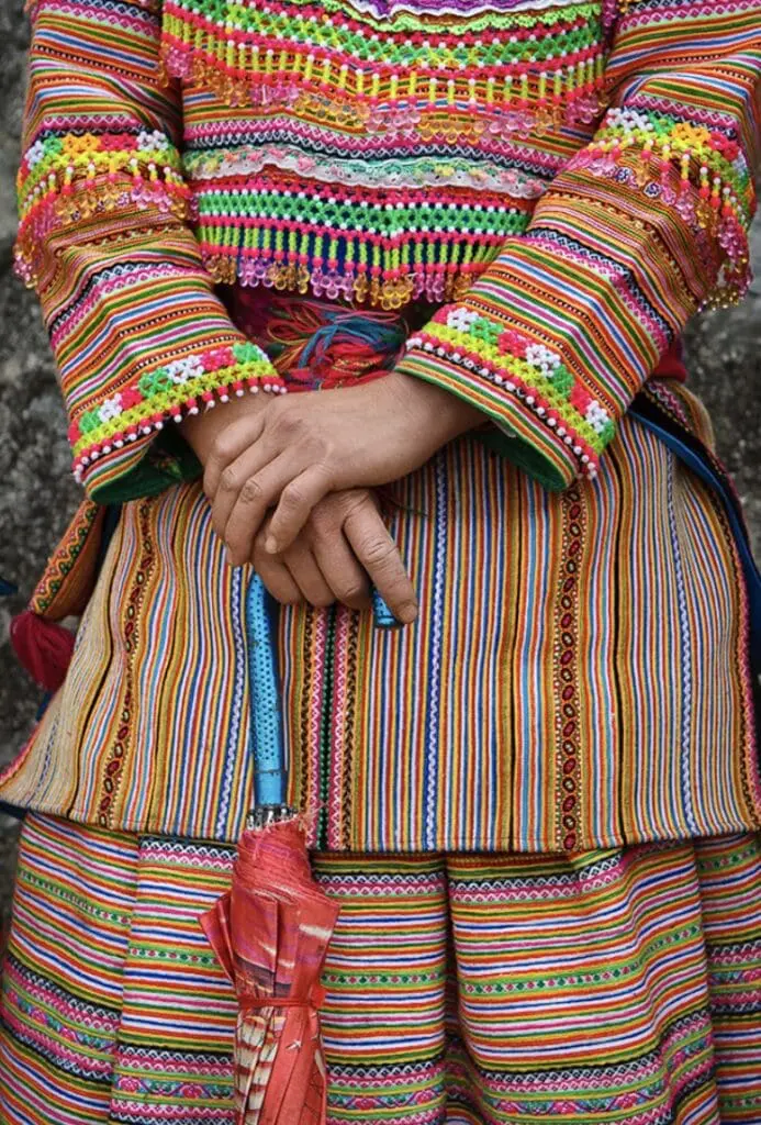 Close-up of a Hmong woman’s hands holding a red umbrella, showcasing intricate embroidery