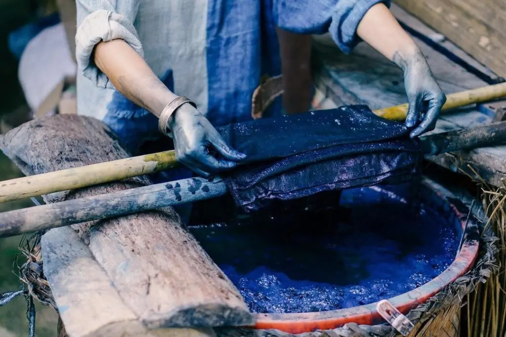 A woman dips fabric into a vat of natural indigo dye