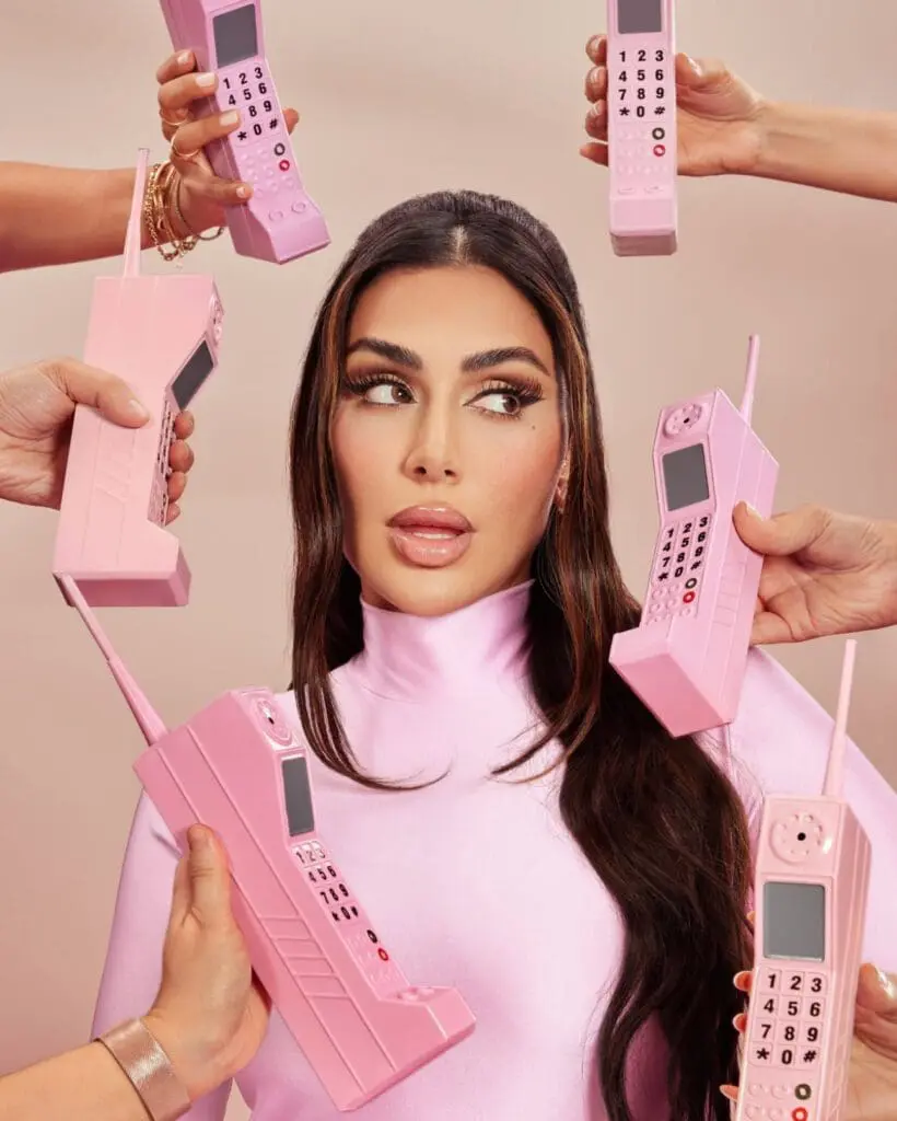 Huda Kattan posing with vintage pink phones around her head