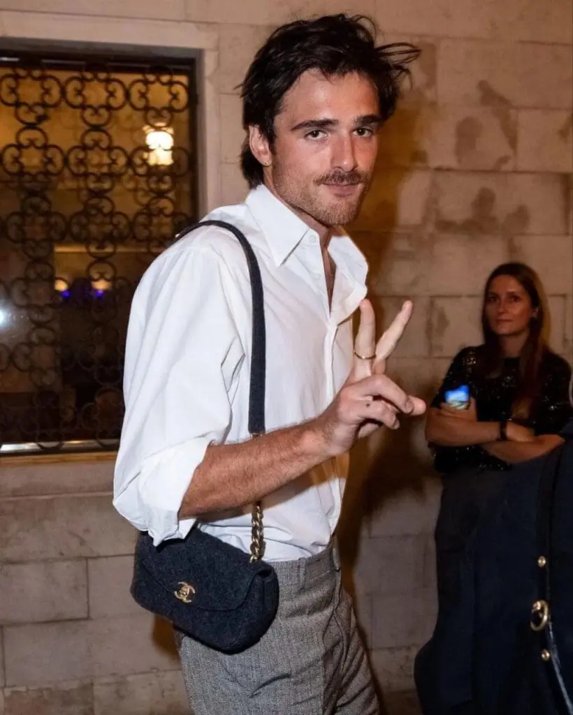 Jacob Elordi wearing a white shirt and Chanel purse, holding up a peace sign