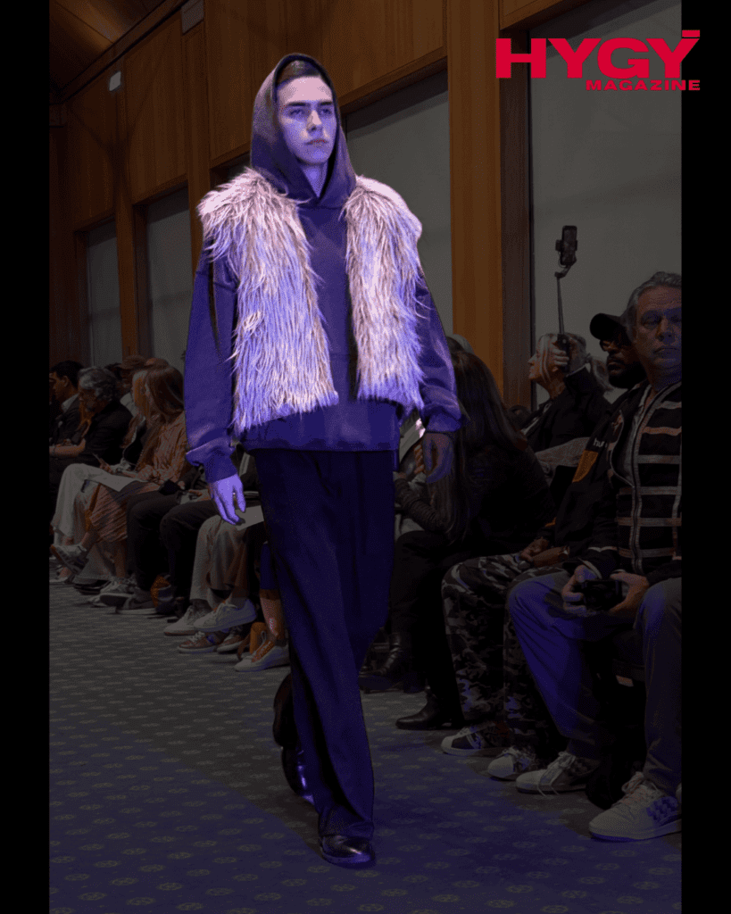 Male model in faux fur vest over hoodie and trousers at graduate show