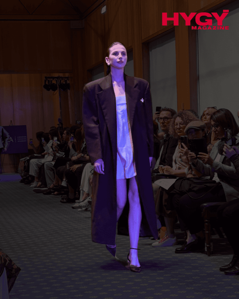 Model in a white mini dress and oversized dark coat on runway