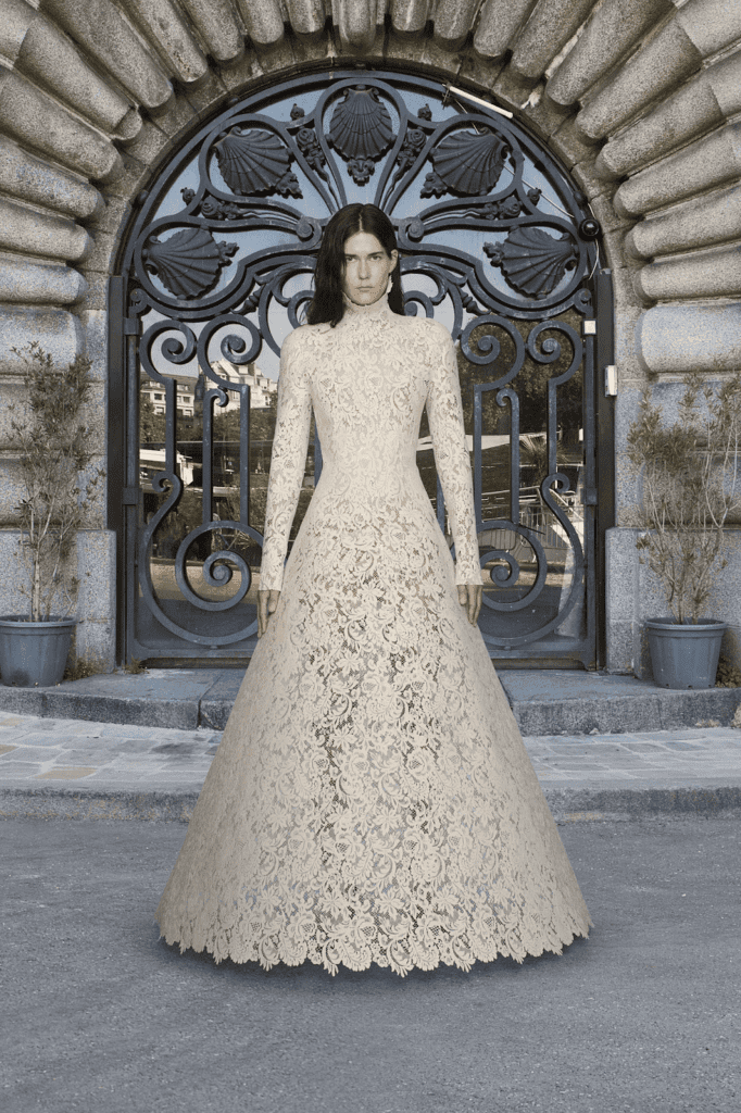 Model wearing intricate floral lace bridal gown in front of an ornate gate