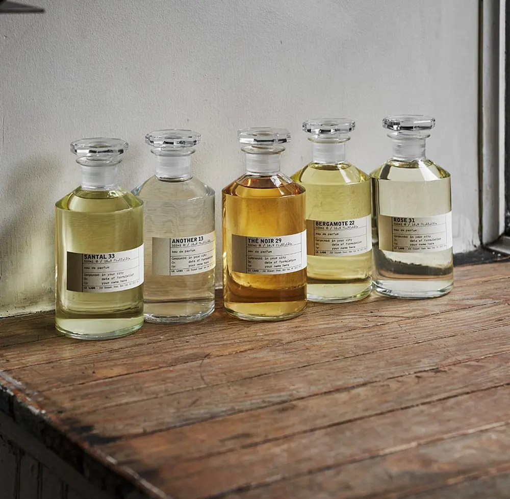 Minimalist Le Labo fragrance bottles lined up on rustic wooden shelf