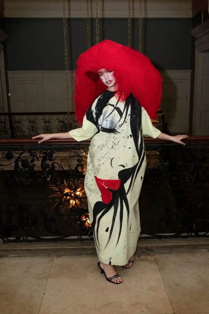 Model in cream dress with black graphic face print and red tulle veil