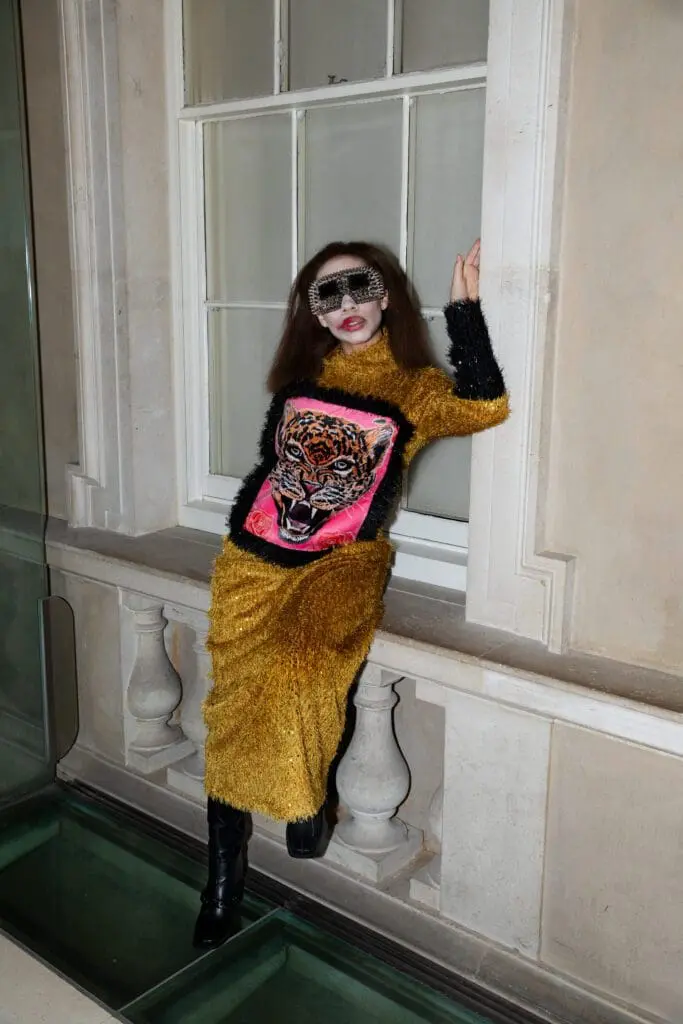 Model in gold textured dress with black sleeves and tiger applique