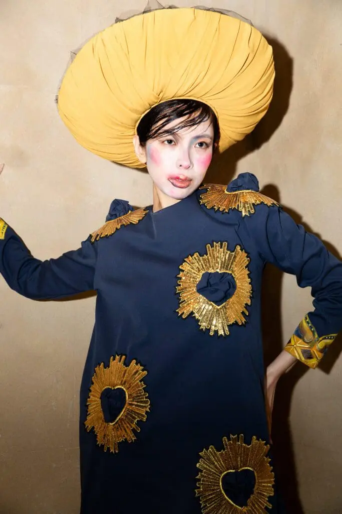 Model in navy dress with gold sunburst appliques and yellow turban hat