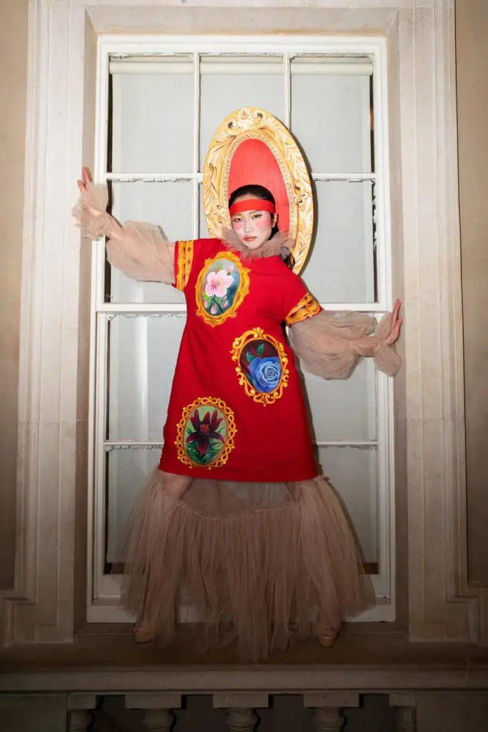 Model in red dress with floral appliqués and gold oval frame headpiece