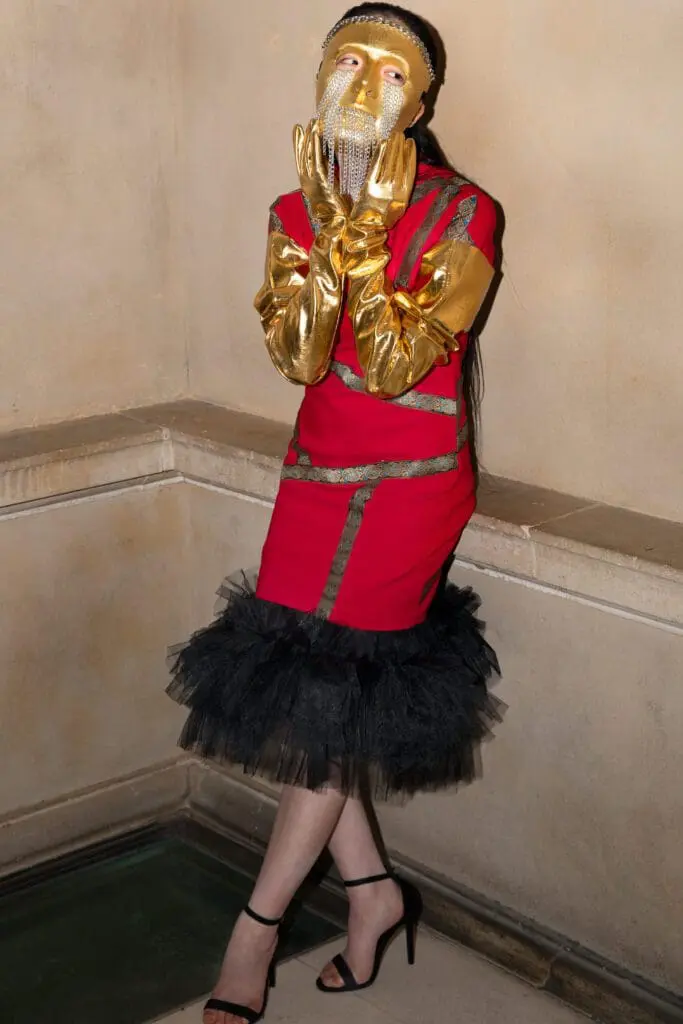 Model in red dress with gold mask, gloves, and black tulle hem