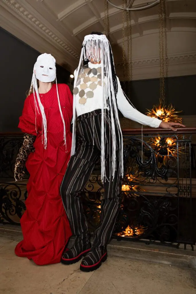 Two models in red dress and striped pants outfits wearing masks