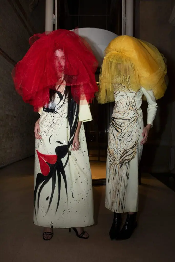 Two models in graphic cream dresses with red and yellow oversized veils
