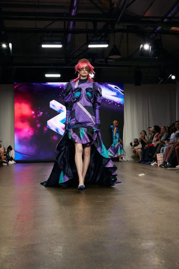 Model in high-low purple and green gown on runway