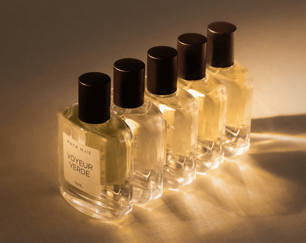 A row of Voyeur Verde perfume bottles glowing under soft light