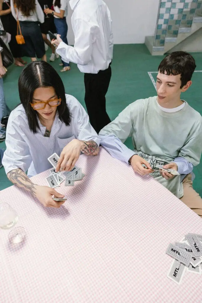 Two male models playing cards at pink checkered table