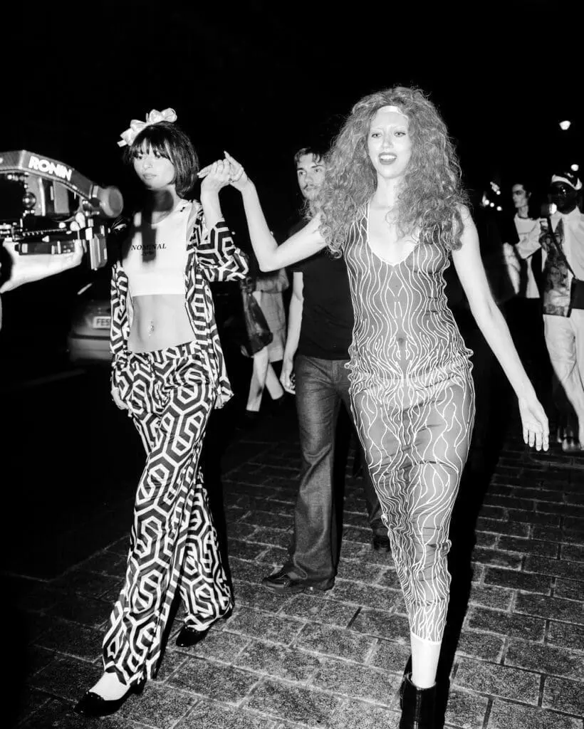 Models walk hand in hand in patterned outfits in black and white image