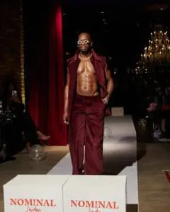 Shirtless model in burgundy velvet pants and vest with layered chains