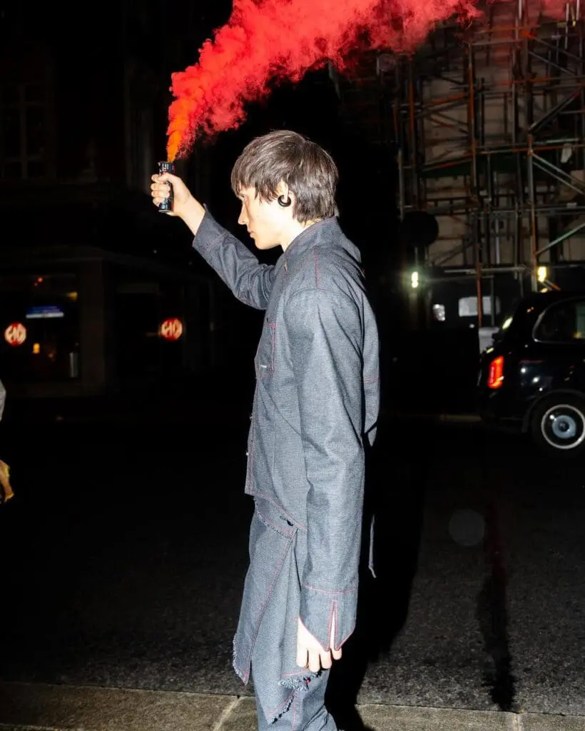 Model with short hair in tailored grey look holding red flare