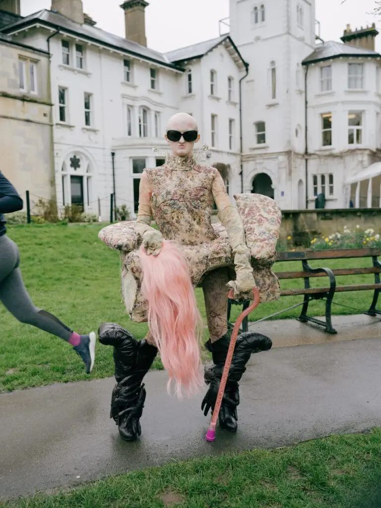 Model Hannah Harpin standing in front of a mansion with pink wig and cane