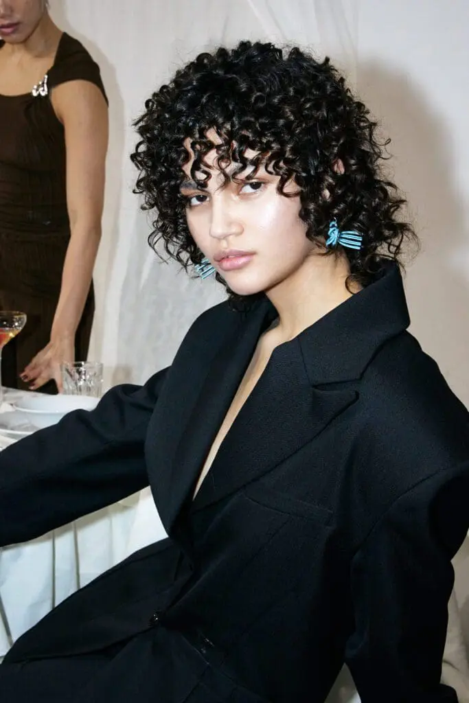 Close-up of model in black blazer with blue earrings