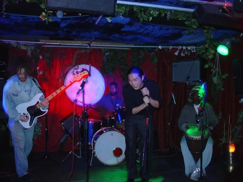 Musicians playing electric guitar, drums, and percussion with vocalist on stage