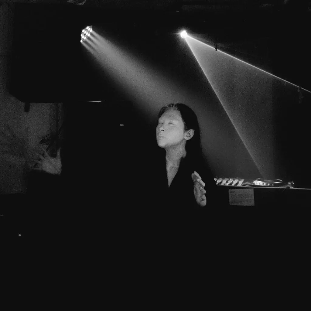 Performer in spotlight with eyes closed, arms raised, bathed in beams of light