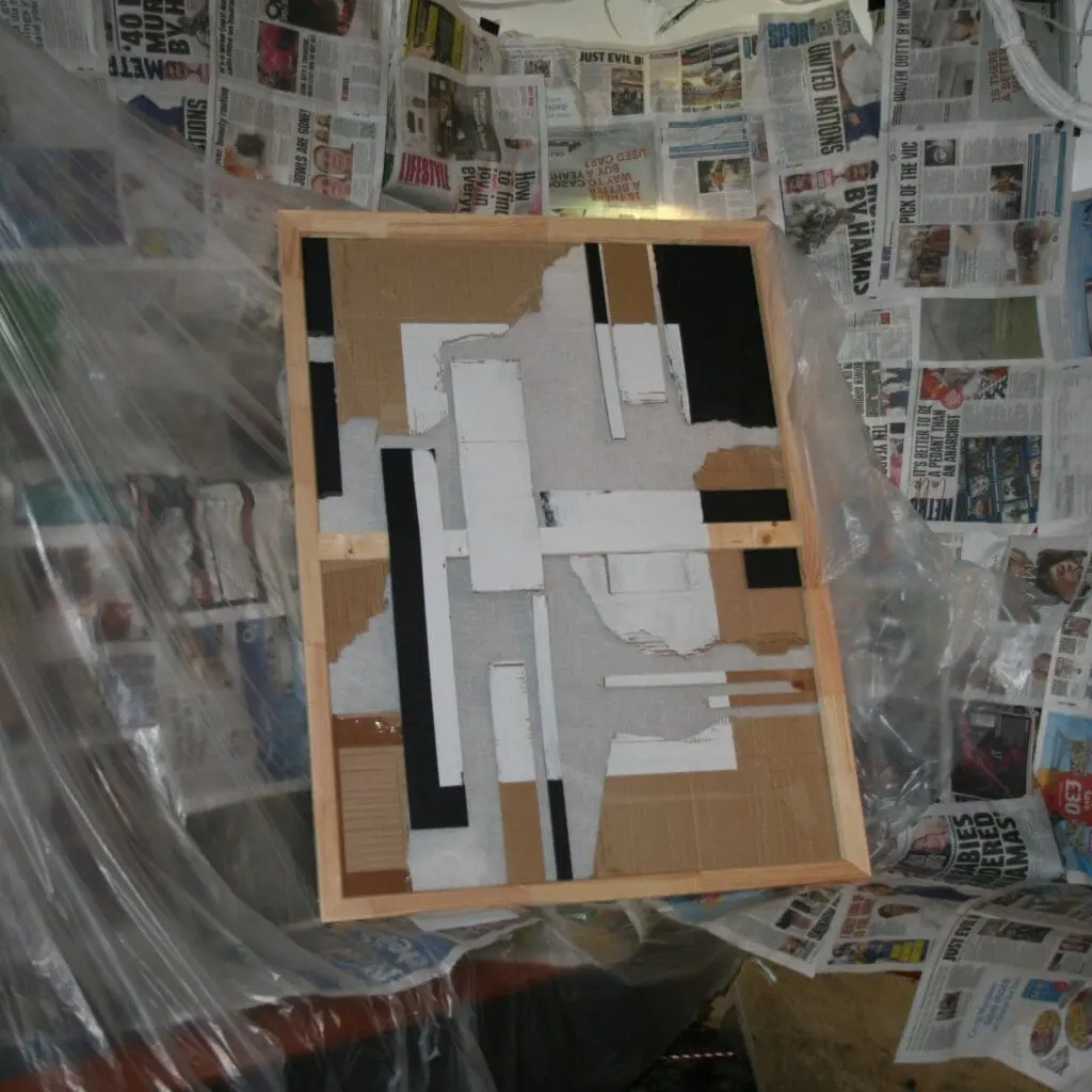 Geometric abstract artwork made with cardboard and tape, surrounded by newspaper-lined walls