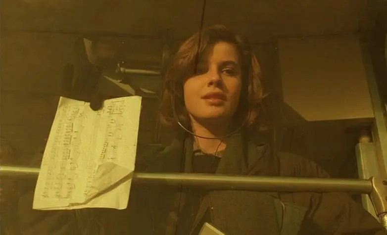 Young woman in headphones looks out from behind a glass window with a musical score taped to it