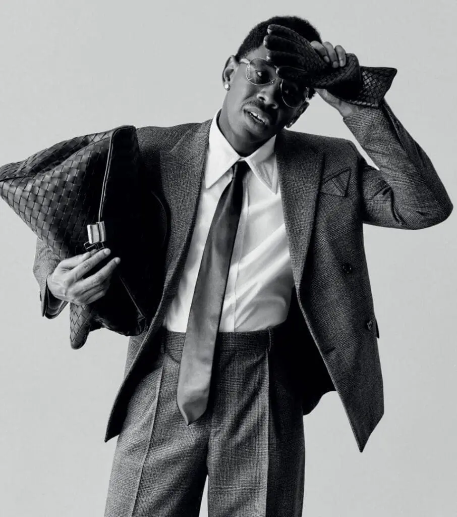 Tyler, The Creator poses in a tailored grey suit with leather gloves and Bottega tote