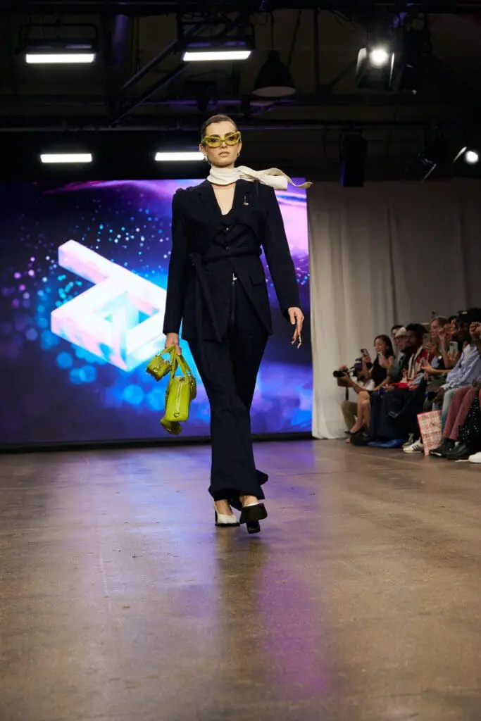 Tailored navy suit with a lime mini bag and yellow sunglasses on the ZIDI runway.