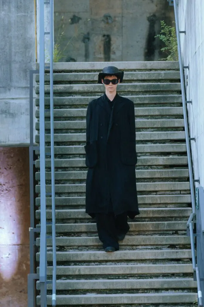 Model in black coat on Sling Stone runway staircase SS26