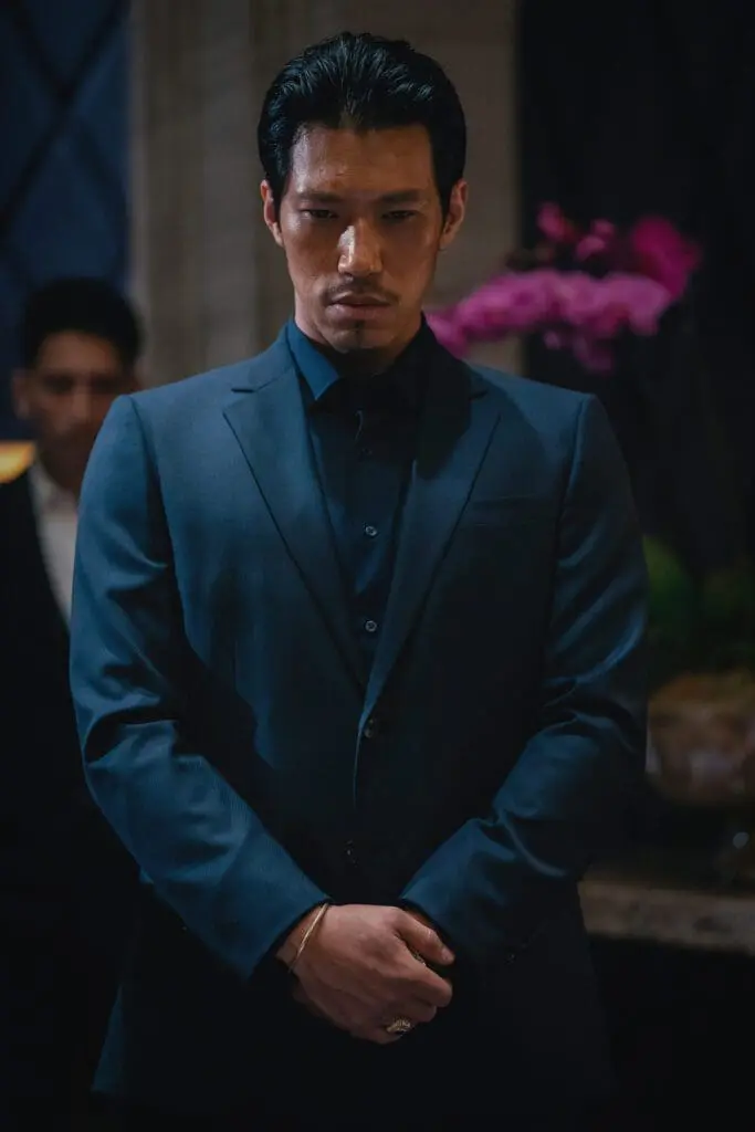 Actor in dark suit standing in dimly lit interior